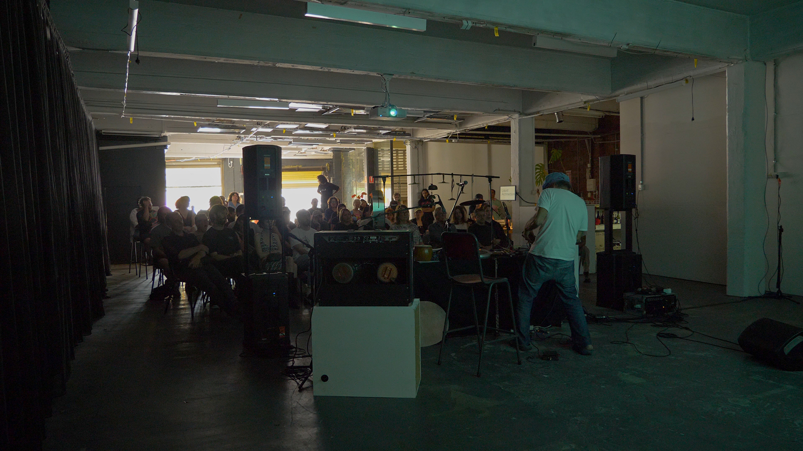 A seated audience watching an artist perform in what seems to be a DIY space